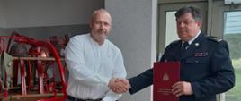 Dyrektor Sprzedaży i Marketingu Członek Zarządu firmy WZ EUROCOPERT Sp. z o. o. w Szczecinku ,stojący z lewej strony, ubrany w białą koszulę, niebieskie spodnie i czarne buty uroczyście przekazuje na ręce Komendanta Powiatowego PSP w Szczecinku bryg. Andrzeja Wójtowicza, ubranego w mundur wyjściowy pilarkę spalinową ratowniczą STIHL. Komendant .