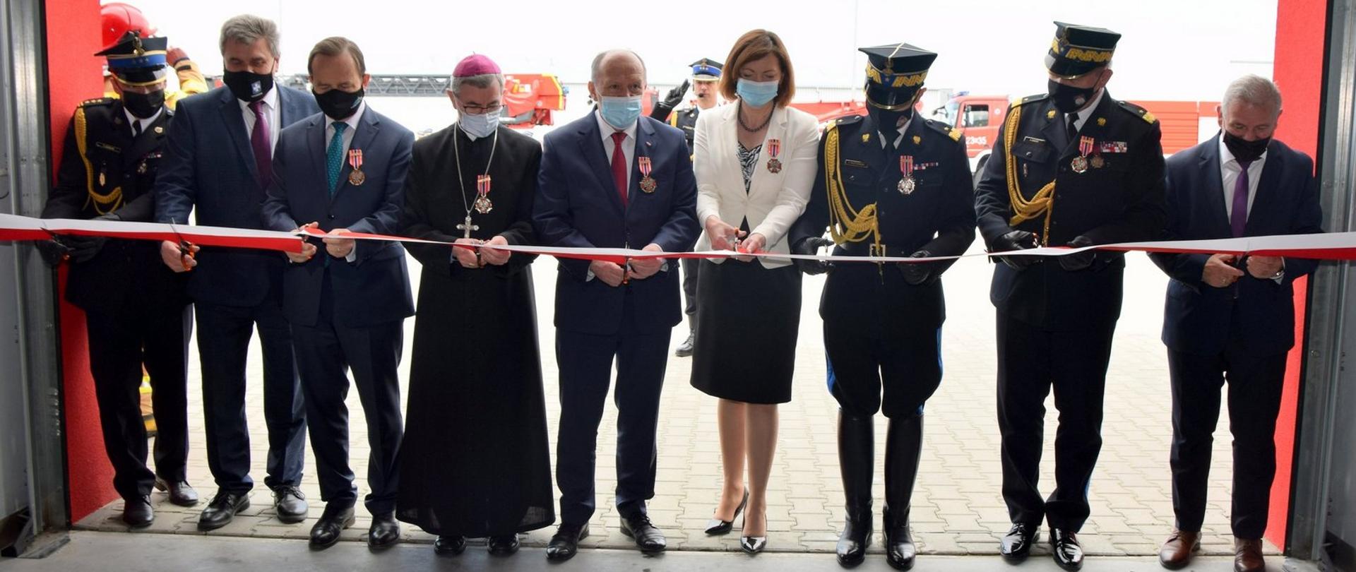 Zdjęcie przedstawia honorowych gości w bramie garażowej na terenie Jednostki Ratowniczo-Gaśniczej Nr 3 w Rzeszowie dokonujących aktu przecięcia wstęgi.