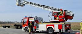 Na zdjęciu drabina mechaniczna oraz strażacy którzy przygotowują się do obsługi i podania wody z kosza drabiny.