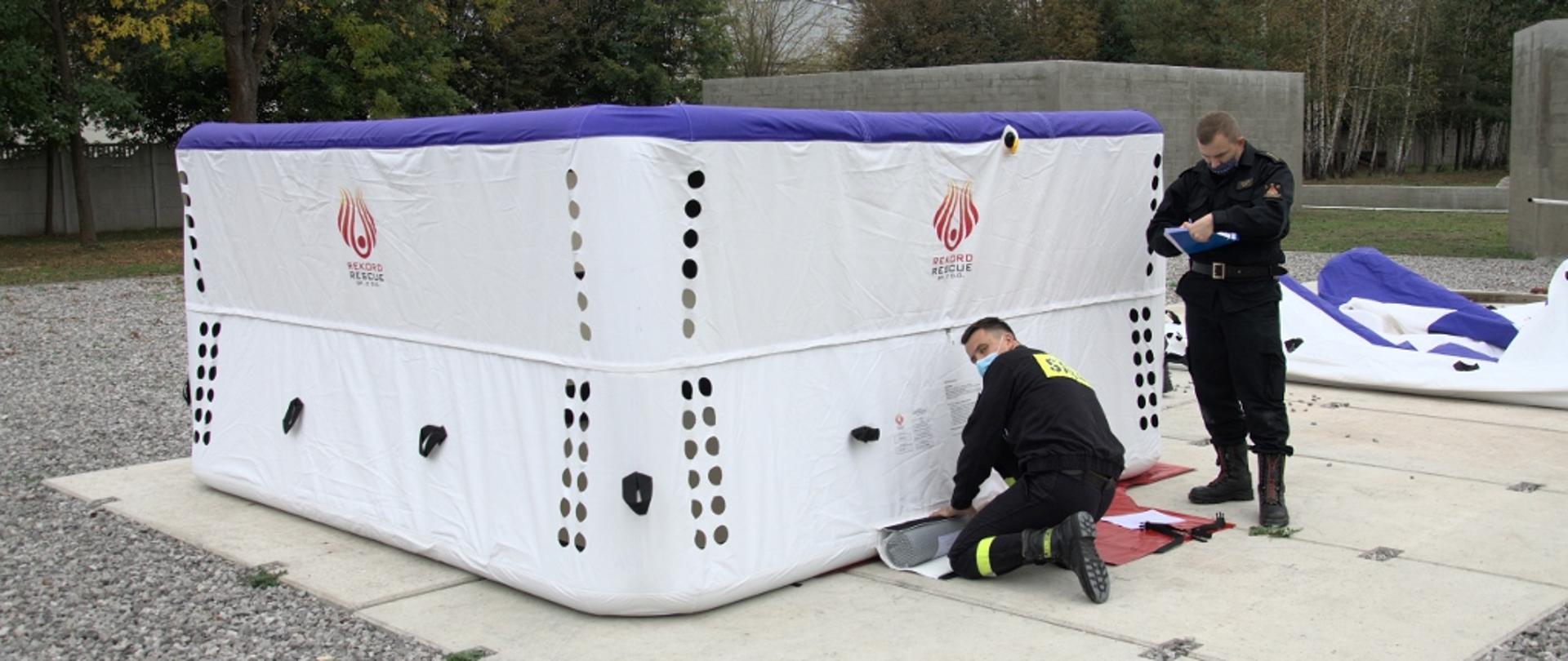 Dwóch funkcjonariuszy PSP przystępują do procedury odbioru skokochronu w kolorze białym.