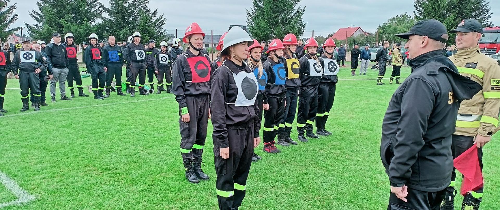 Na zdjęciu dowódca Ochotniczej Straży Pożarnej Ratownik druhna Karolina Drażdżewska składająca meldunek do brygadiera Pawła Puchowskiego.
W tle Strażacy biorący udział w zawodach
