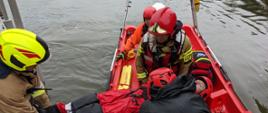 Strażacy przenoszący pozorowanego poszkodowanego z łodzi na brzeg jeziora podczas ćwiczeń