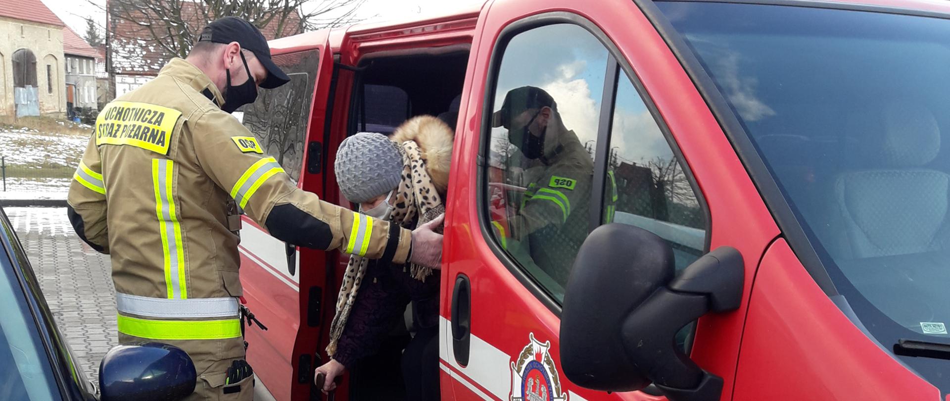 Strażak pomaga starszej kobiecie wysiąść z samochodu. 
