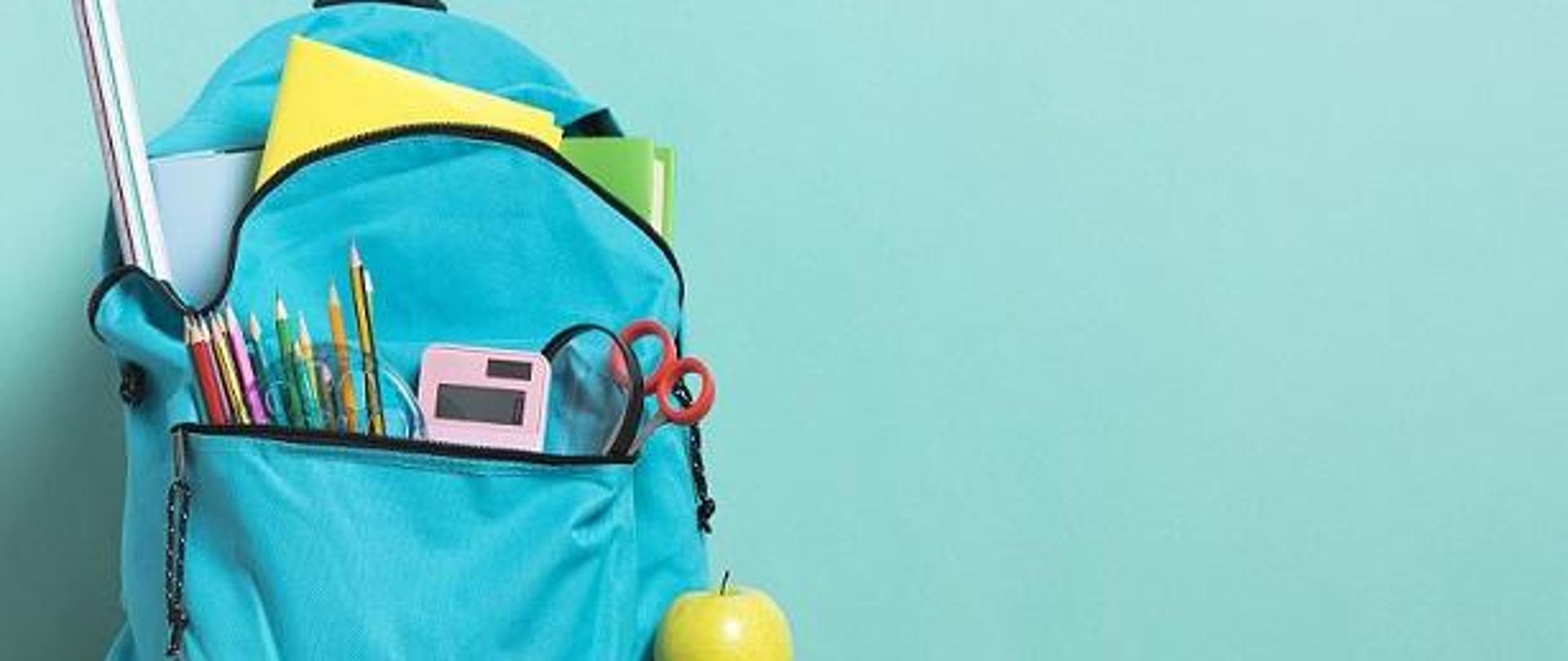 plecak szkolny stojący na podłodze, z kieszonki wystają przybory szkolne