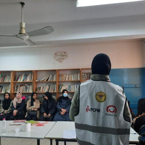 W sali siedzą kobiety w hidżabach i słuchają instruktorki prowadzącej szkolenie