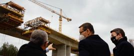 Minister Adamczyk pokazuje premierowi i rzecznikowi palcem budowę.