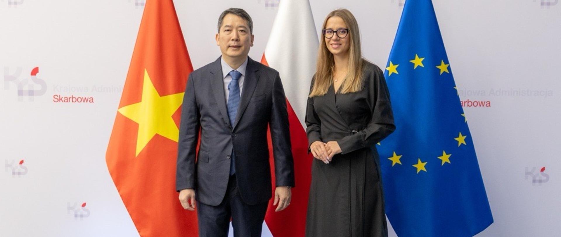 Zastępca Szefa Krajowej Administracji Skarbowej Małgorzata Krok z wiceministrem finansów Wietnamu Cao Anh Tuấn. W tle flaga Polskie, UE i Wietnamu.