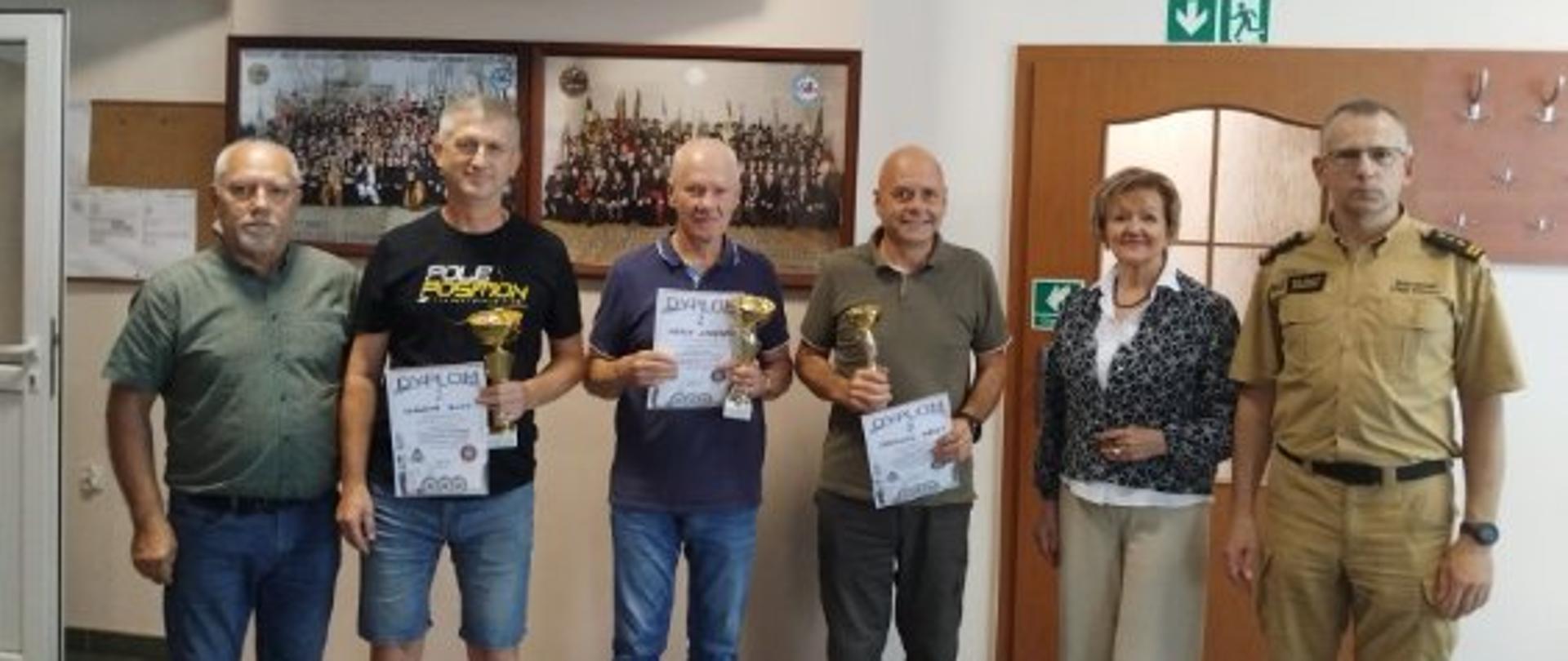 grupa osób stojących z pucharami i dyplomami