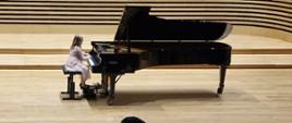 Dziewczynka w bladoróżowej tiulowej sukience gra na fortepianie Fazioli.