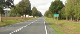 Na zdjęciu widoczna droga, po jednym pasie w każdym kierunku. Poza jezdnią widoczne drzewa rosnące przy drodze. Po prawej stronie widoczny las oraz znak informujący o tym, że za 13 kilometrów jest miejscowość Piła. 