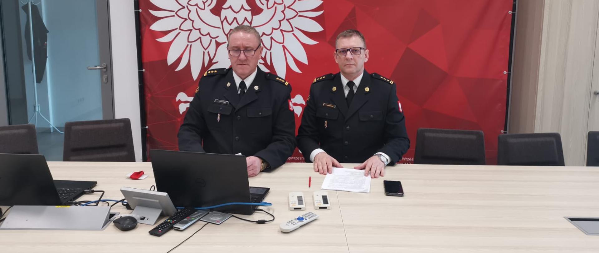 Zdjęcie przedstawia dwóch komendantów powiatowych z laptopem na tle godła państwowego