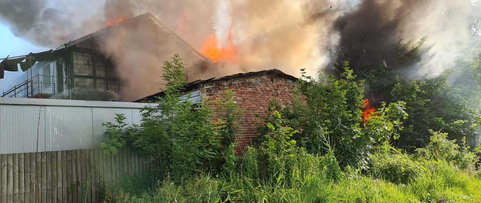 Widok budynku gospodarczego z widocznymi płomieniami. Dookoła panuje duże zadymienie.