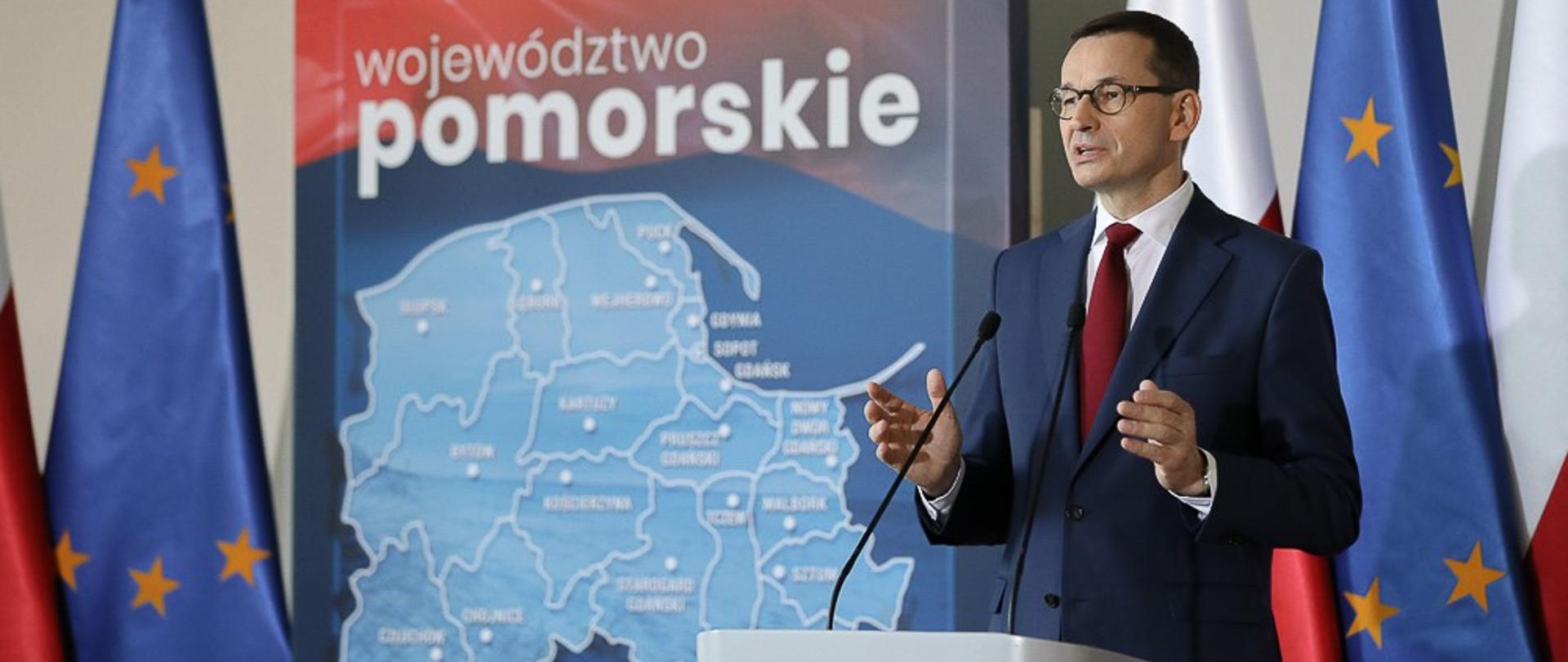 Premier Mateusz Morawiecki przemawia na tle mapy województwa pomorskiego.