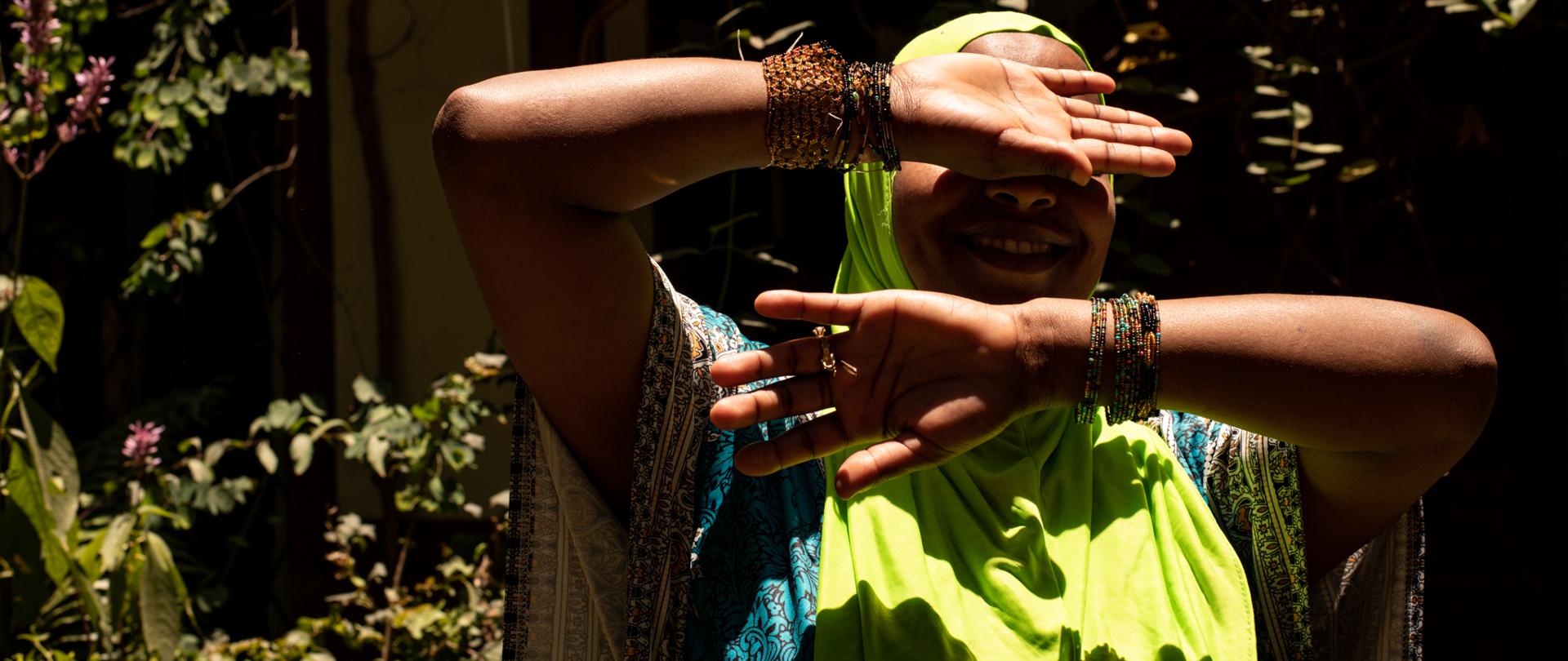 Kobieta stojąca w ostrym słońcu, zasłaniająca ręką górną część twarzy.