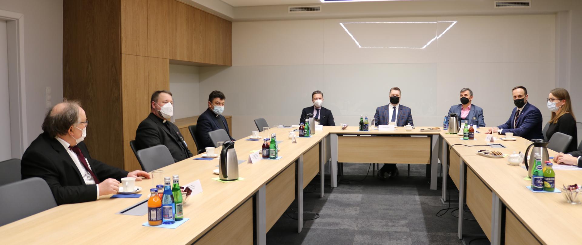 Minister Przemysław Czarnek siedzi przy stole z innymi uczestnikami spotkania.