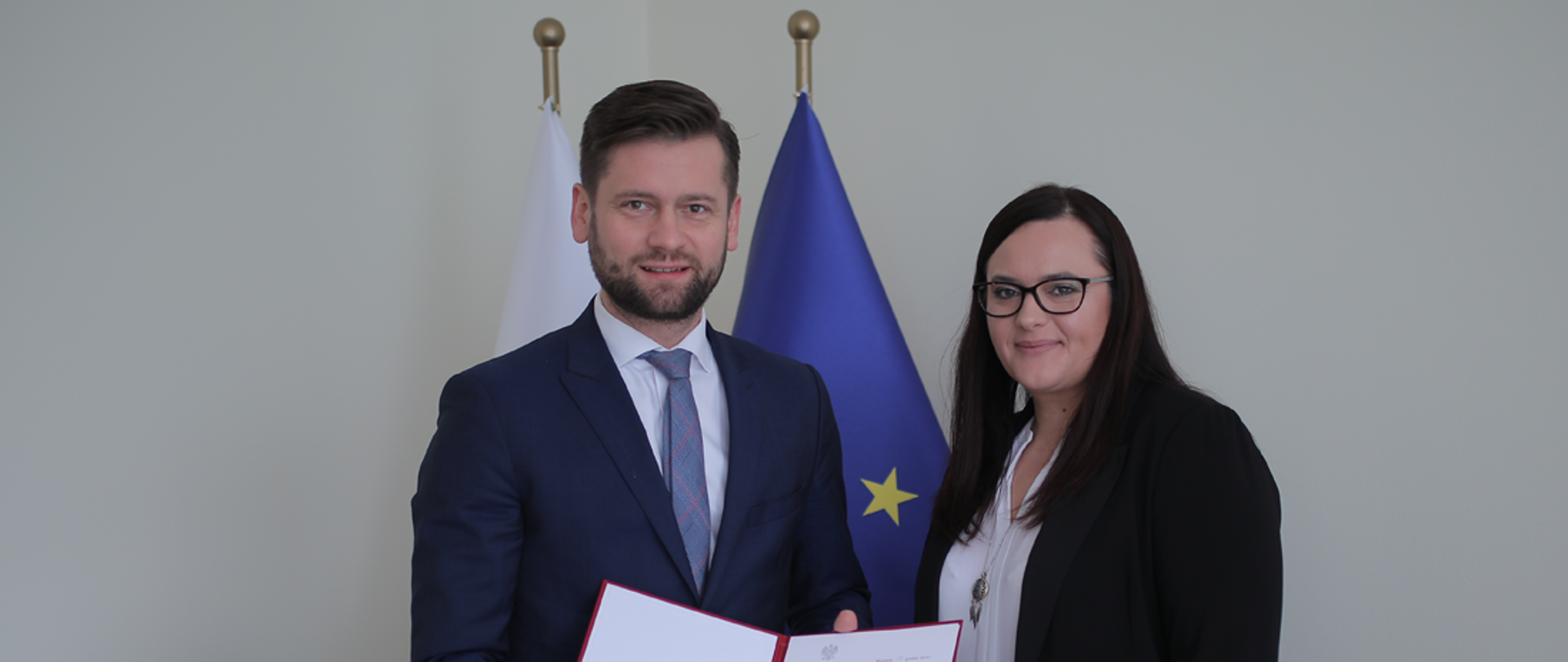 Na tle flag Polski i UE stoi minister Małgorzata Jarosińska-Jedynak oraz nowy wiceminister funduszy i polityki regionalnej Kamil Bortniczuk