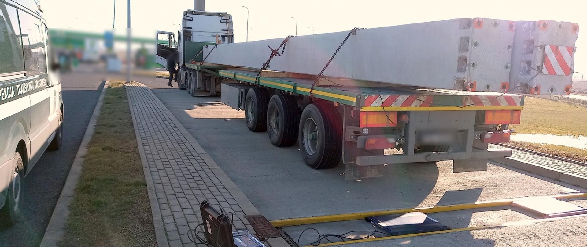 Ciężarówka przewożąca dwa betonowe słupy stoi tuż za przenośnymi wagami ITD.