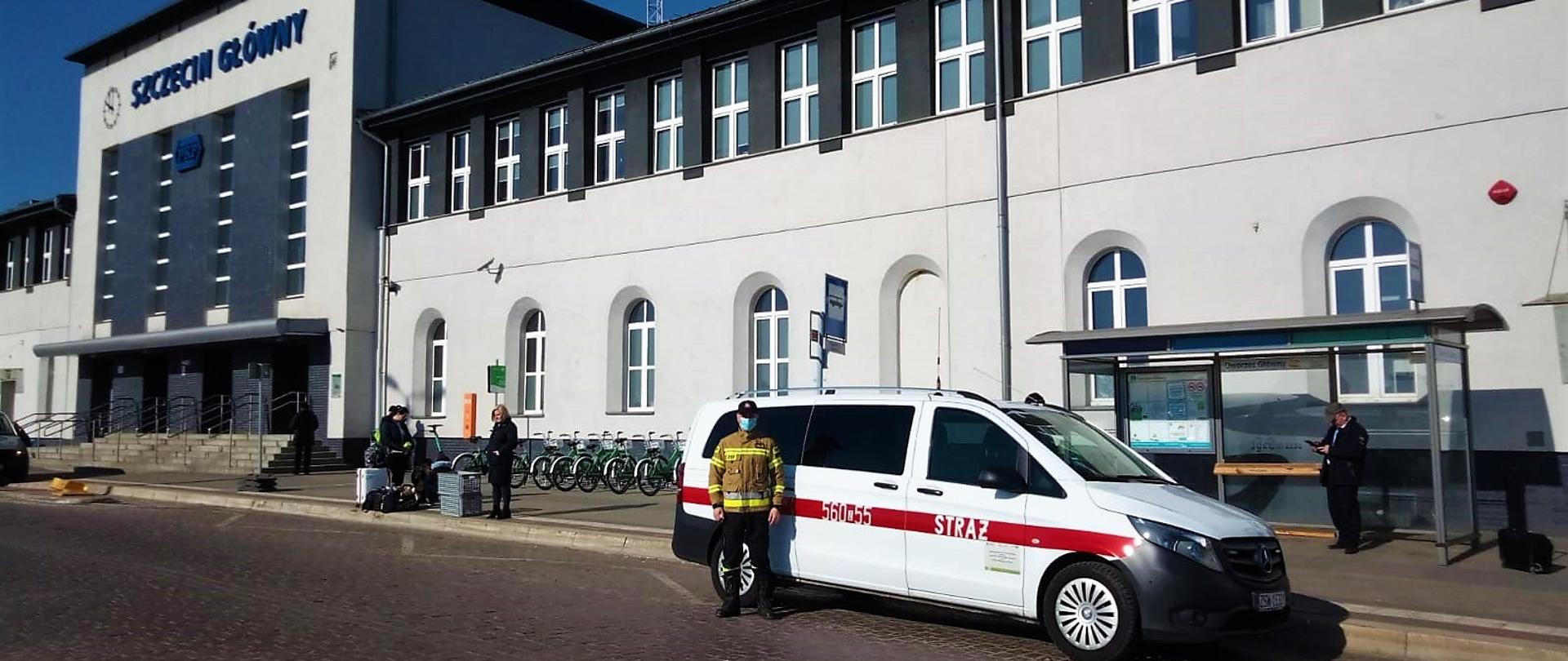 Bus w kolorze białym z KM PSP w Świnoujściu na tle Dworca Głównego PKP w Szczecinie. Stoi przy nim strażak w kurtce koloru piaskowego.