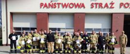 Na zdjęciu przed KP PSP w Środzie Wlkp. widać strażaków OSP, którzy ukończyli szkolenie kierowców-konserwatorów sprzętu ratowniczego OSP oraz dwóch funkcjonariuszy PSP. Zdjęcie wykonane na zewnątrz budynku przed bramami garażowymi Komendy.