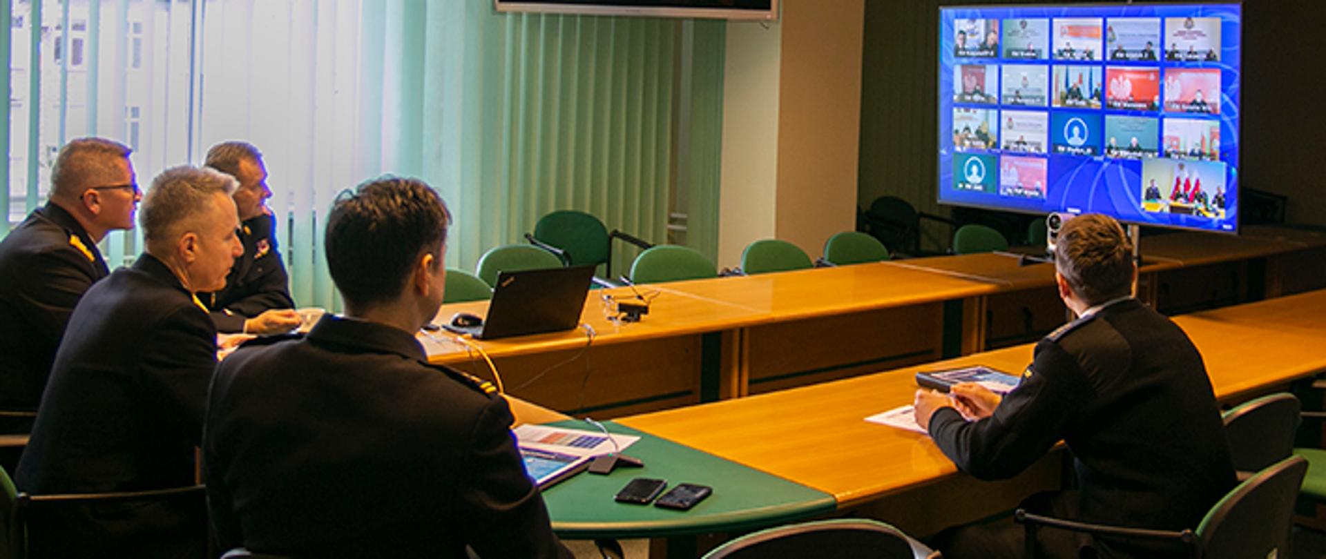 Kierownictwo Komendy Głównej Państwowej Straży Pożarnej podczas wideokonferencji. W tle terminal wideokonforencyjny