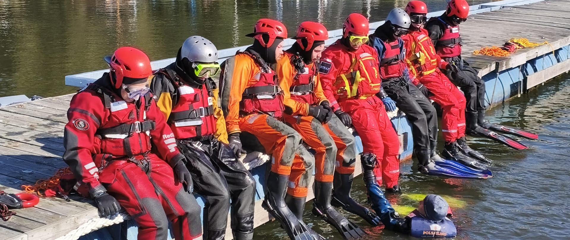 Na zdjęciu strażacy podczas szkolenia na jeziorze, strażacy stoją na pomoście i ćwiczą wejście do wody