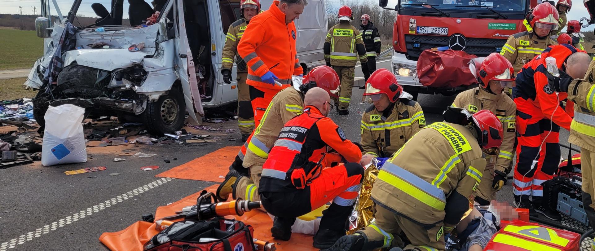 Strażacy i ratownicy pomagają poszkodowanemu w wypadku w tle uszkodzony pojazd