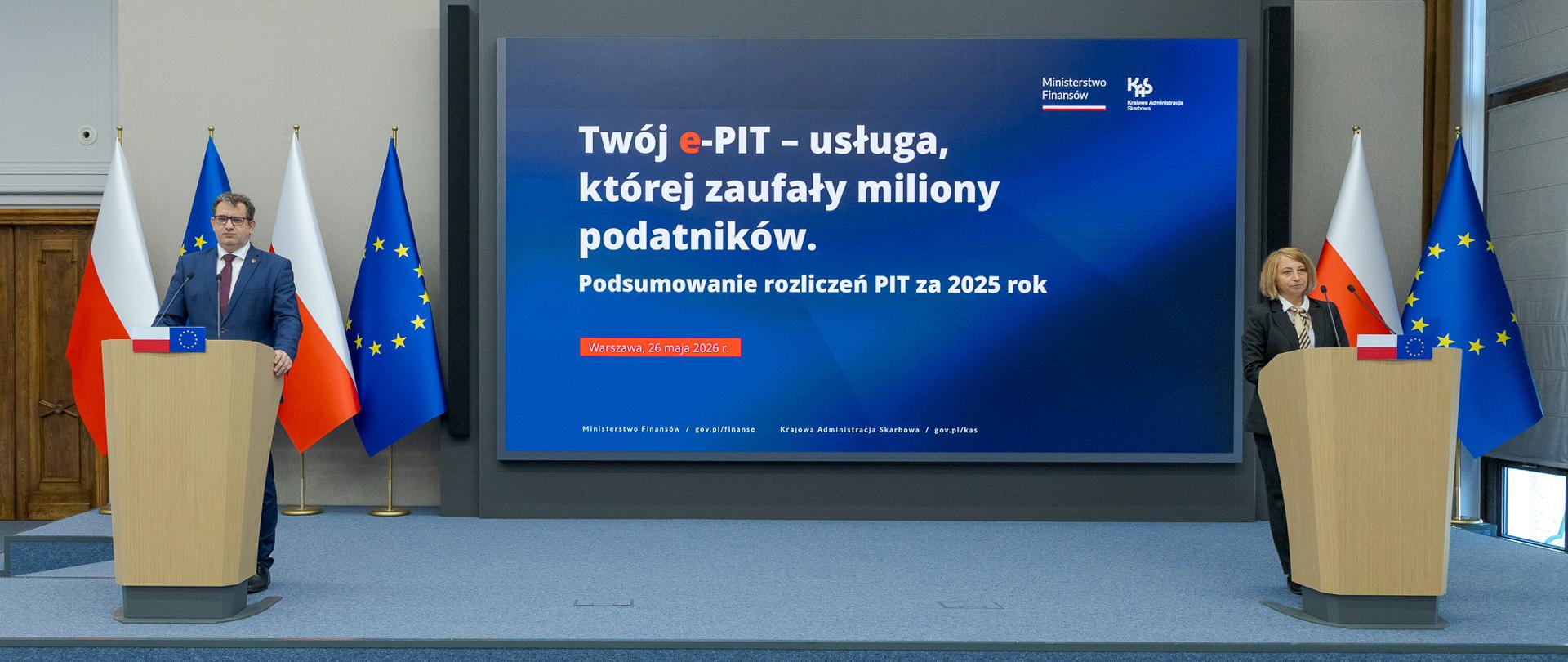 Dwie osoby stoją przy oddzielnych mównicach, a między nimi ekran z napisem „Twój e‑PIT – usługa, której zaufały miliony podatników” oraz informacją o podsumowaniu PIT za 2025 rok.
