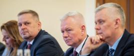 Zdjęcie wykonane podczas spotkania w Pałacu Prezydenckim w Baku. Na zdjęciu 4 osoby siedzące przy stole – 3 mężczyzn i jedna kobieta. Pierwszy po prawej minister Tomasz Siemoniak. Na stole szklanki, butelki z wodą, materiały. W prawym dolnym rogu widać kobiece dłonie. W tle żółta ściana i drzwi.