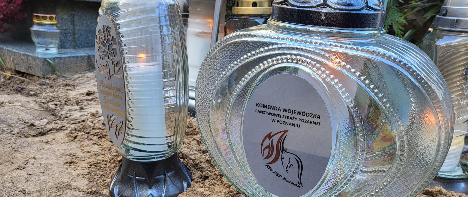 Zdjęcie przedstawia znicze z logotypem Komendy Wojewódzkiej PSP w Poznaniu ustawione przed grobem.