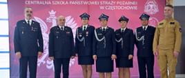 Od lewej stojący Zastępca Komendanta Centralnej Szkoły PSP, następnie Komendant Centralnej Szkoły PSP, kolejno trzy druhny OSP, dalej druh OSP oraz funkcjonariusz CS PSP na tle czerwonego baneru CS PSP