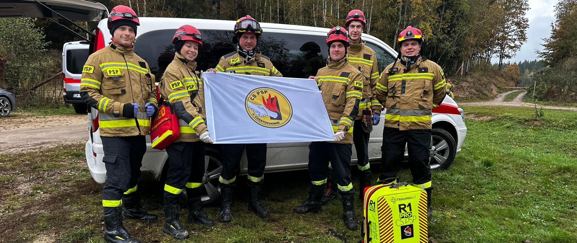 Leśna polana, pamiątkowe zdjęcie grupowe kadetki, czterech kadetów oraz strażaka CS PSP trzymających białą flagę z logo CS PSP