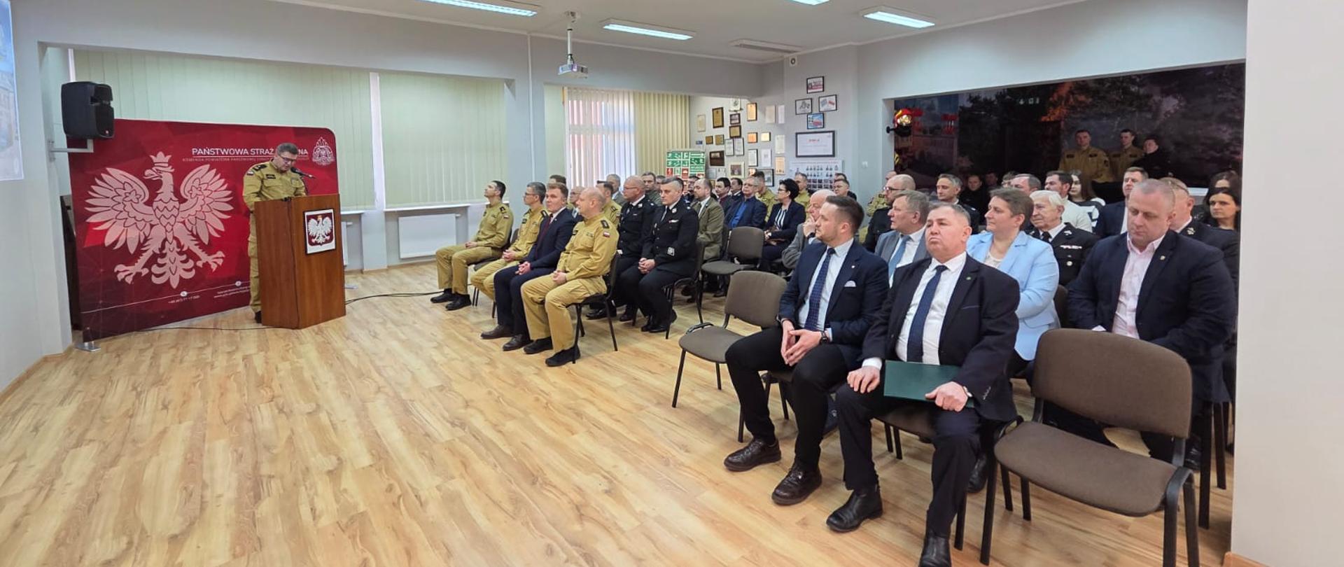 Zdjęcie przedstawia strażaków podsumowujących działalność Komendy za rok 2024.
W tle świetlica i baner Komendy Powiatowej Państwowej Straży Pożarnej w Chodzieży.
