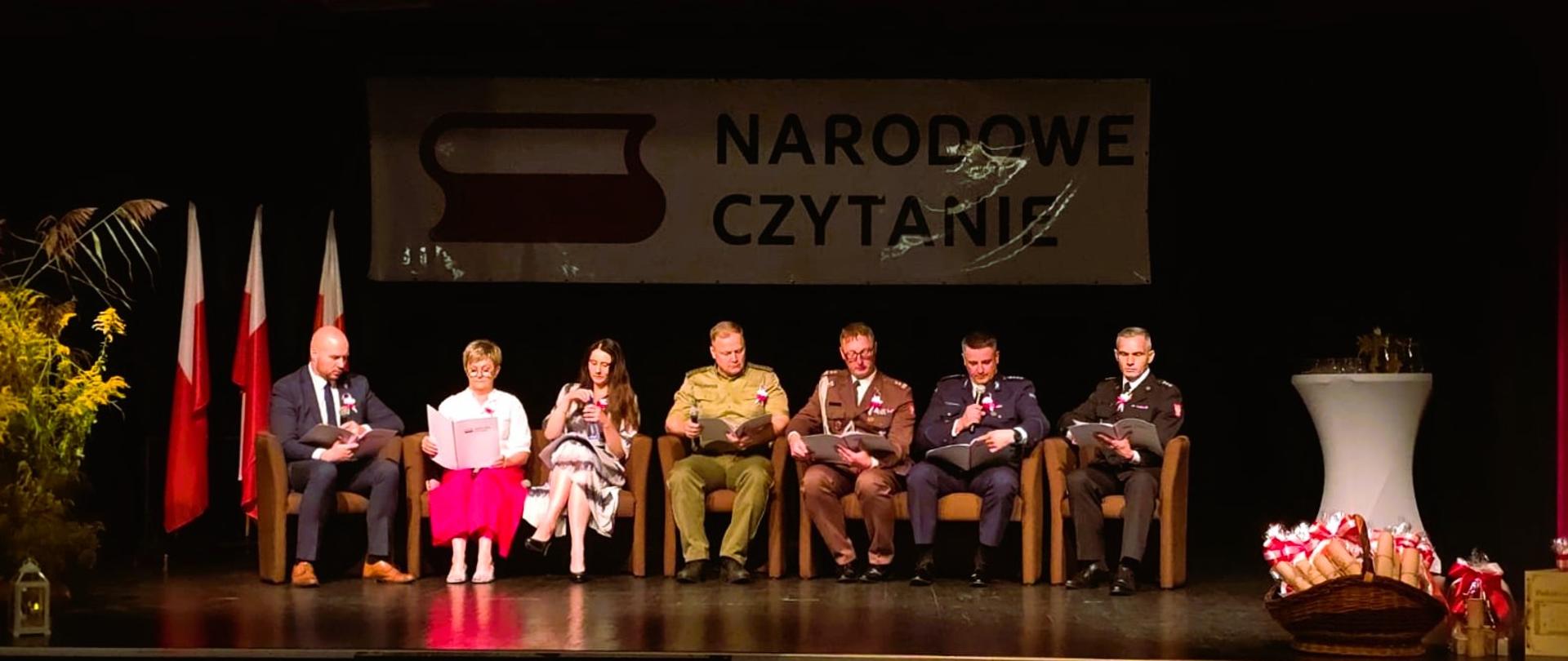 Zdjęcie przedstawia uczestników ogólnopolskiej akcji Narodowe Czytanie 2025 zlokalizowanych na scenie kina "Kultura" w Gołdapi. Pierwszy z prawej to funkcjonariusz Komendy Powiatowej Państwowej Straży Pożarnej w Gołdapi kpt. Daniel Żamojtuk