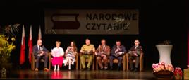 Zdjęcie przedstawia uczestników ogólnopolskiej akcji Narodowe Czytanie 2025 zlokalizowanych na scenie kina "Kultura" w Gołdapi. Pierwszy z prawej to funkcjonariusz Komendy Powiatowej Państwowej Straży Pożarnej w Gołdapi kpt. Daniel Żamojtuk
