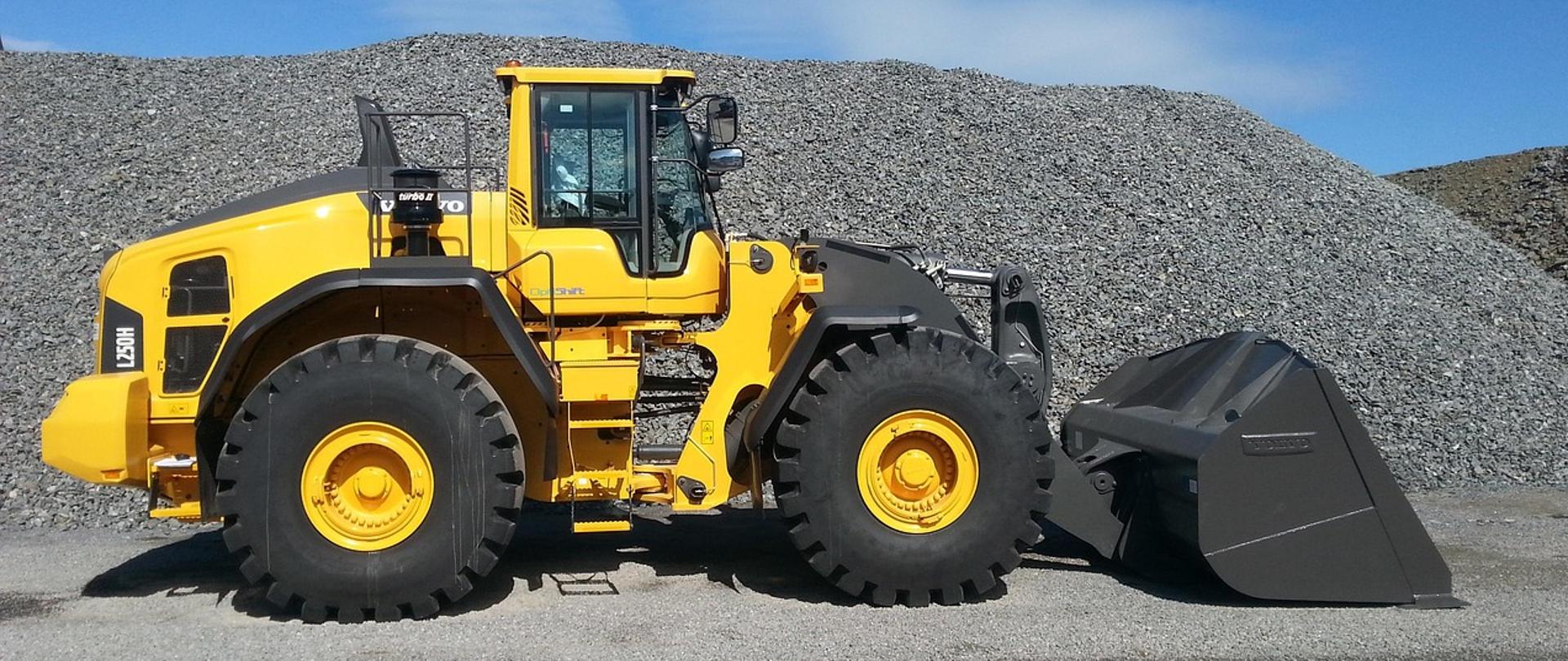 Koparko – ładowarka w kolorze żółtym na tle żwiru