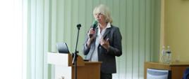 Na zdjęciu widać Dyrektor Wydziału Zdrowia OUW Mirosławę Kwatek-Hoffmann. Stoi przy mównicy, trzyma w ręku mikrofon i mówi do uczestników narady. 