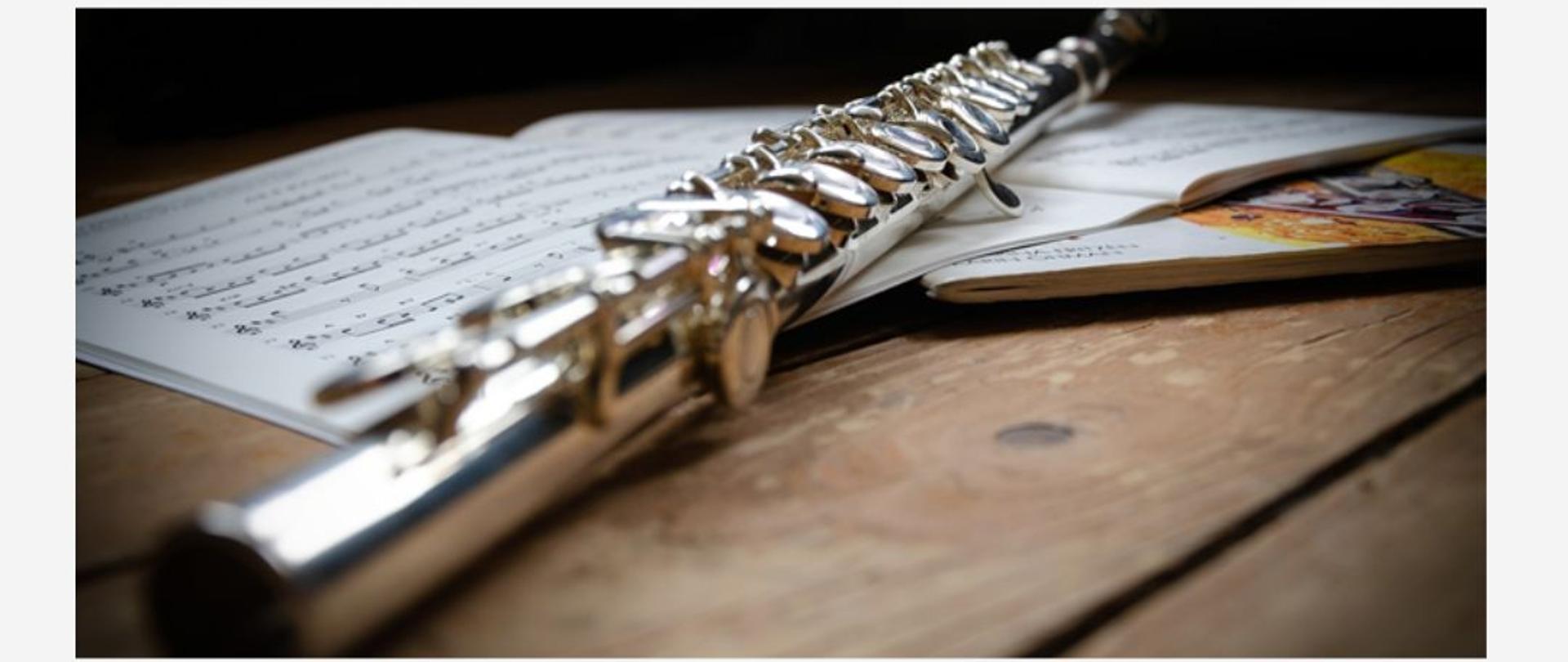 Plakat przedstawia zdjęcie fletu położonego na drewnianym blacie, obok niego leżą nuty oraz informację, że Audycja klasy fletu Pani Marii Daszkowskiej odbędzie się 15 maja 2025 r o godzinie 17:30 w sali koncertowej PSM I st.w Płońsku.