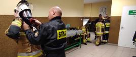 Strażak ratownik OSP pomaga ubierać się druhowi w aparat układu oddechowego przed wejściem do komory dymowej