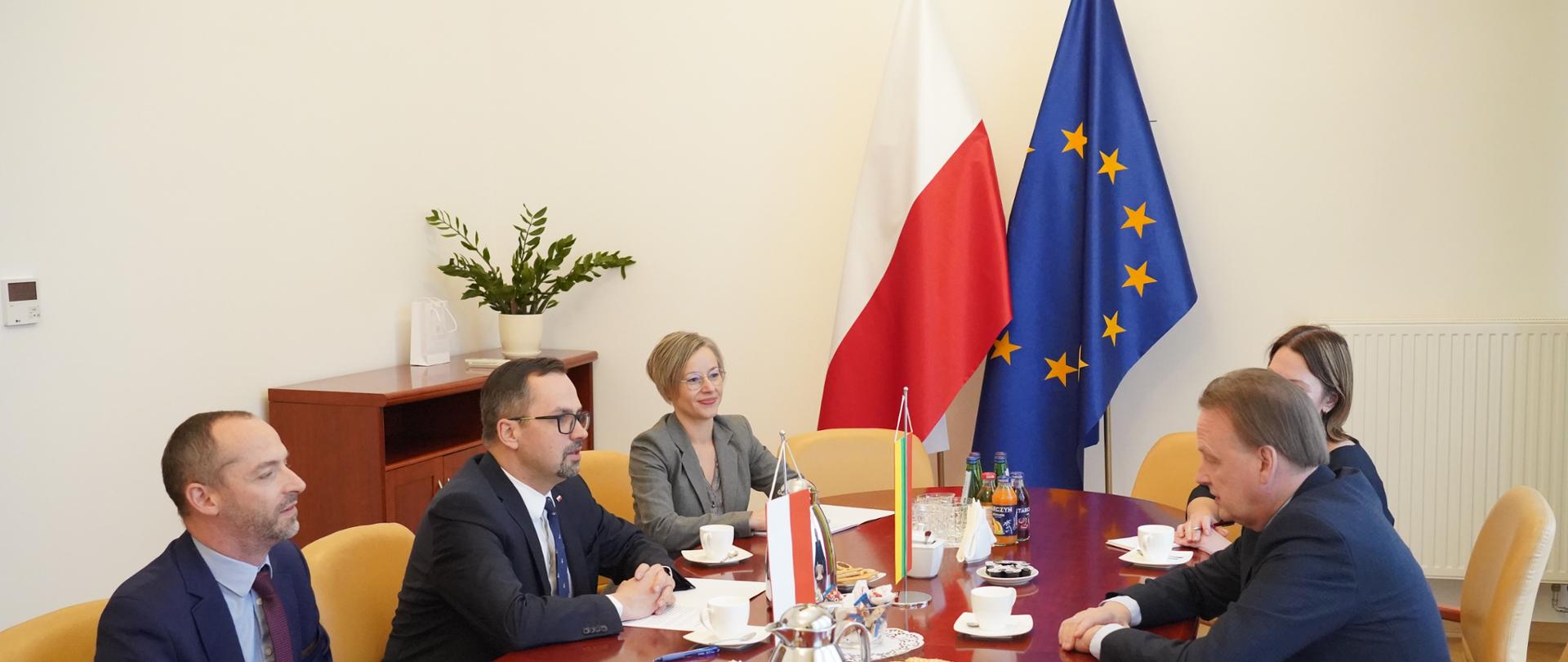 Pięć osób siedzi przy stole. Drugi od lewej siedzi wiceminister Marcin Horała. W środku na stole stoją dwie małe flagi Polski i Litwy.