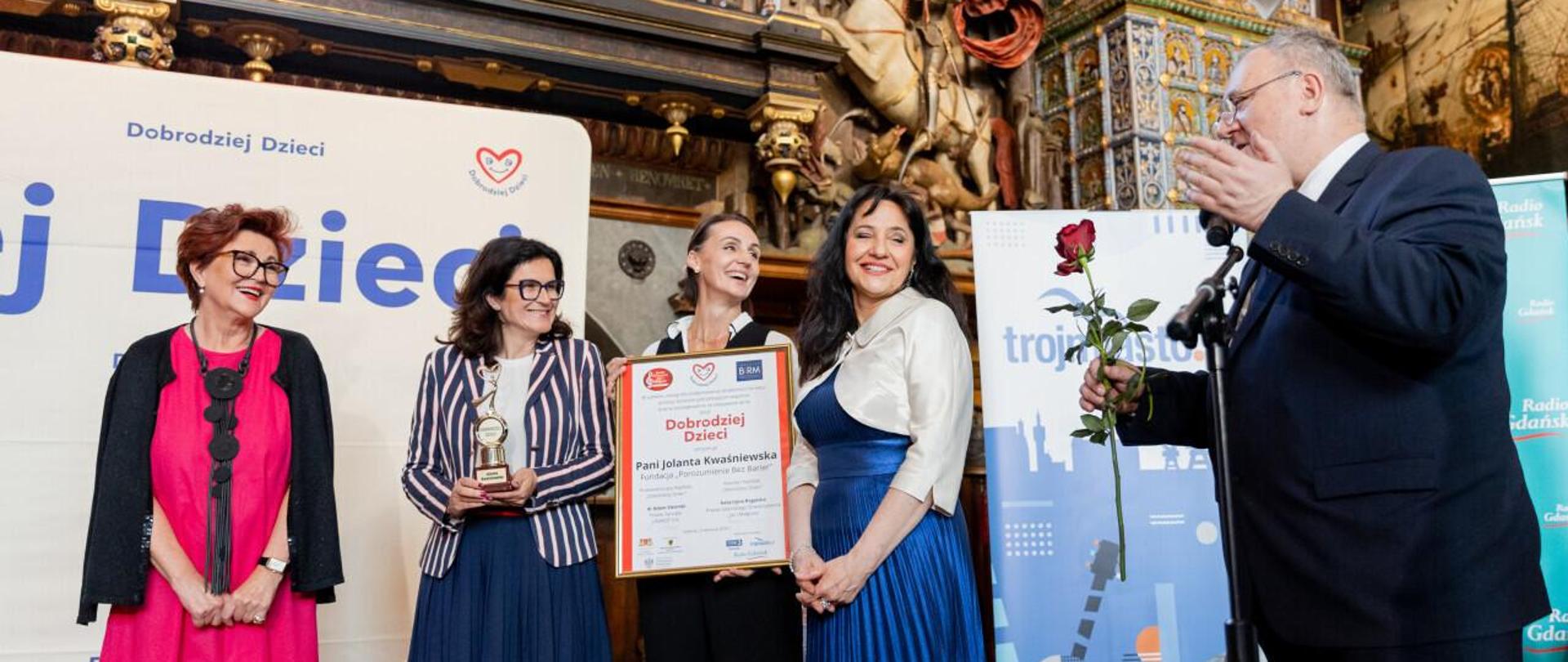 Grupa uśmiechniętych osób stoi przed banerem Dobrodziej dzieci