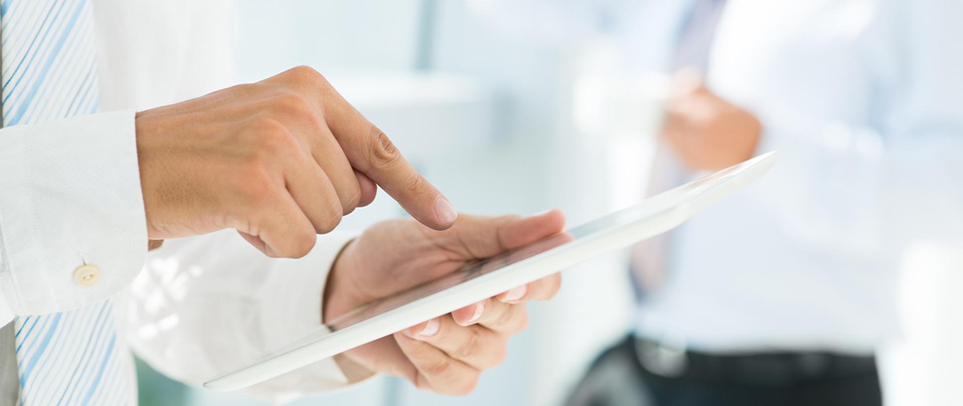 Przedsiębiorcy otrzymali 140 mld zł z tarczy antykryzysowej - Grafika z dłonią trzymającą tablet