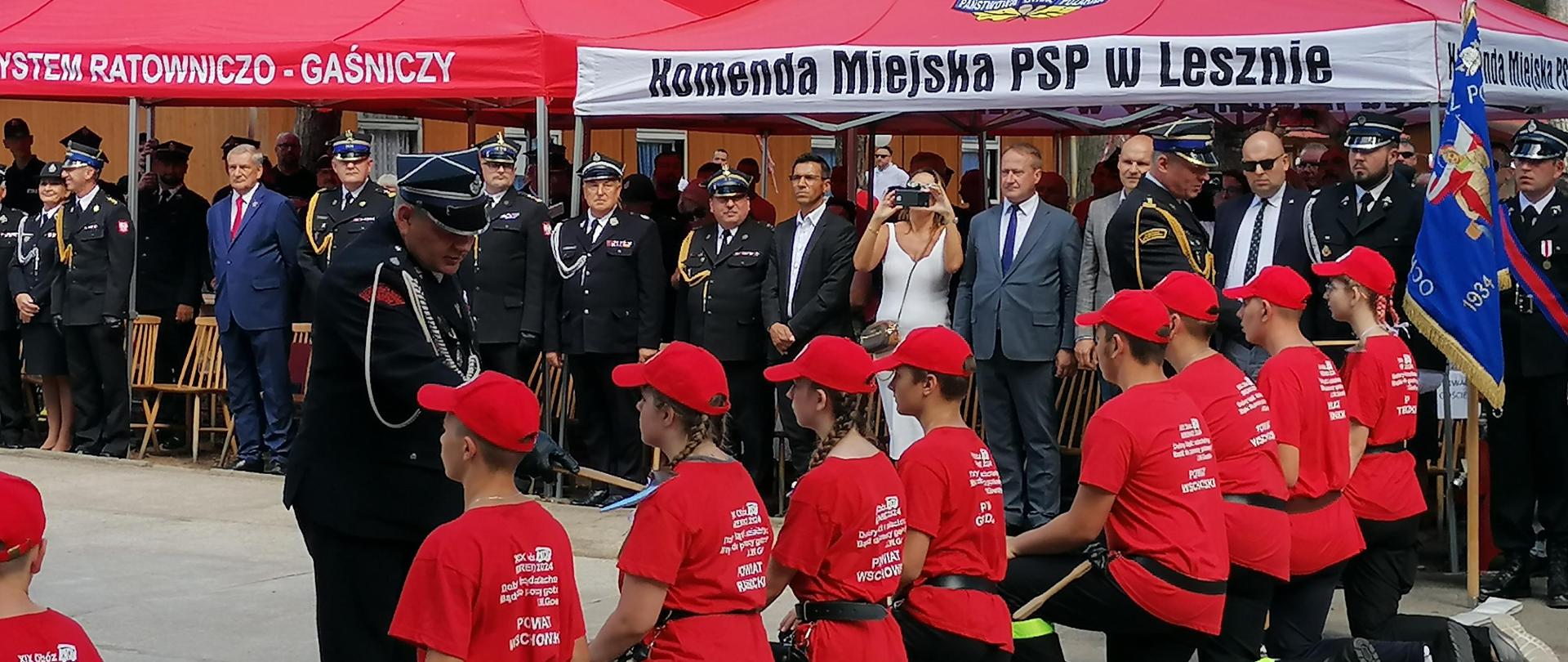 Młodzież klęczy na placu strażacy za pomocą toporka nominują ich na młodych strażaków.