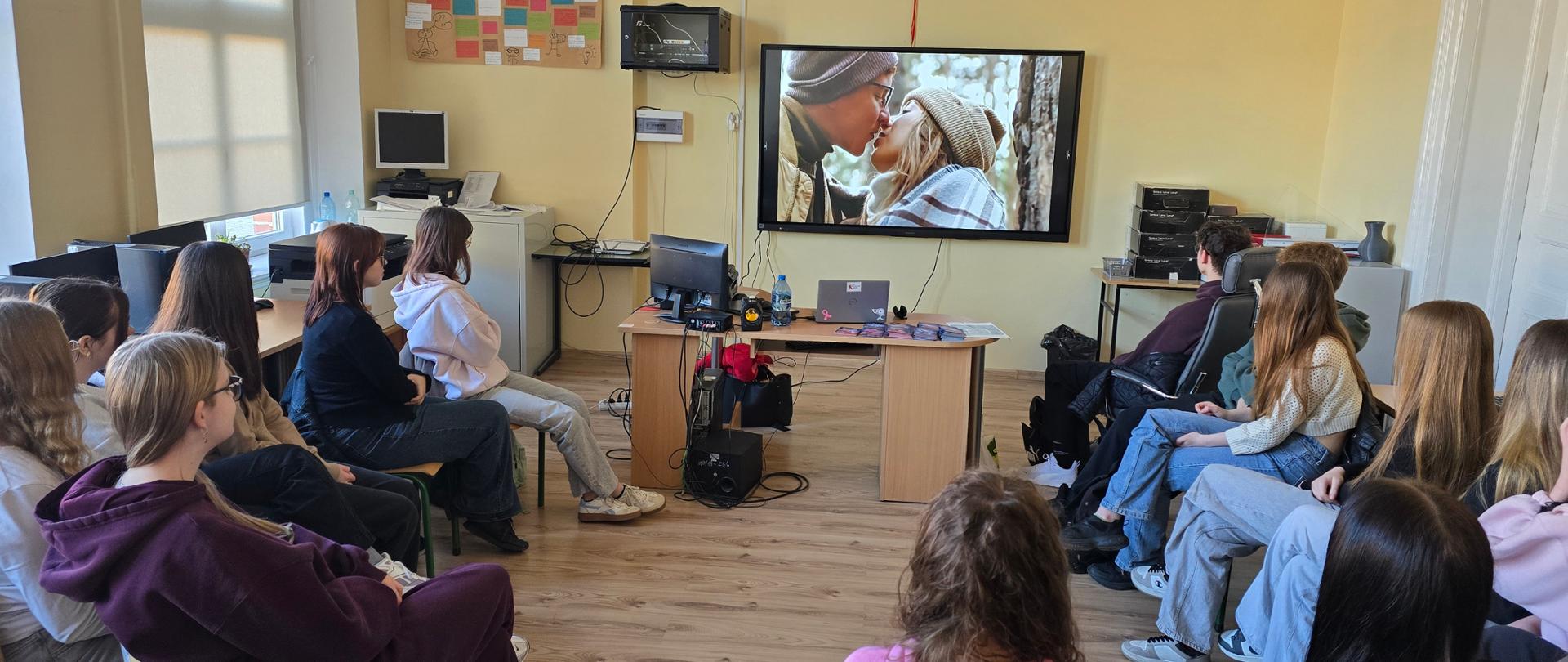 grupa młodzieży w sali lekcyjnej oglądająca film