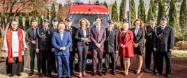 zaproszeni gości pozują do zdjęcia na placu przed remizą podczas uroczystości Przekazania samochodu do OSP Przewóz, w tle samochód pożarniczy
