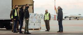 Rozładunek paczek na płycie lotniska. Przesyłkę oglądają premier Mateusz Morawiecki, minister Adam Niedzielski oraz Michał Kuczmierowski.