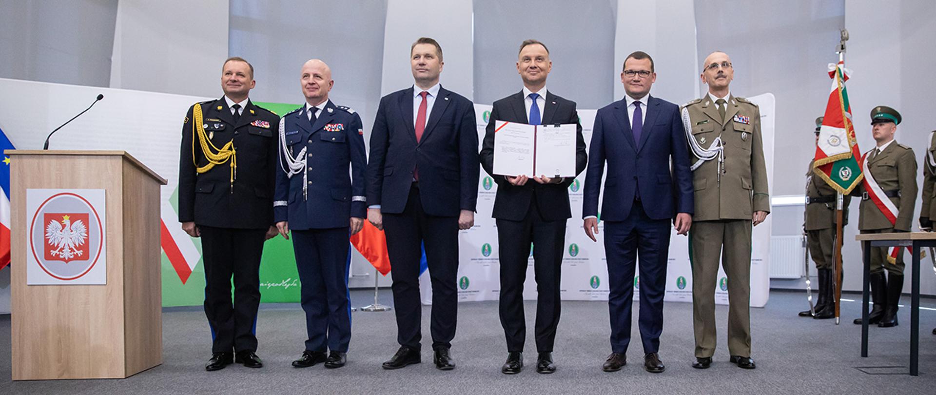 Zdjęcie prezydenta Andrzeja Dudy z podpisaną ustawą, wiceministra Pawła Szefernakera, ministra Przemysława Czarnka, komendanta Tomasza Pragi, komendanta Jarosława Szymczyka i zastępcy komendanta Adama Koniecznego