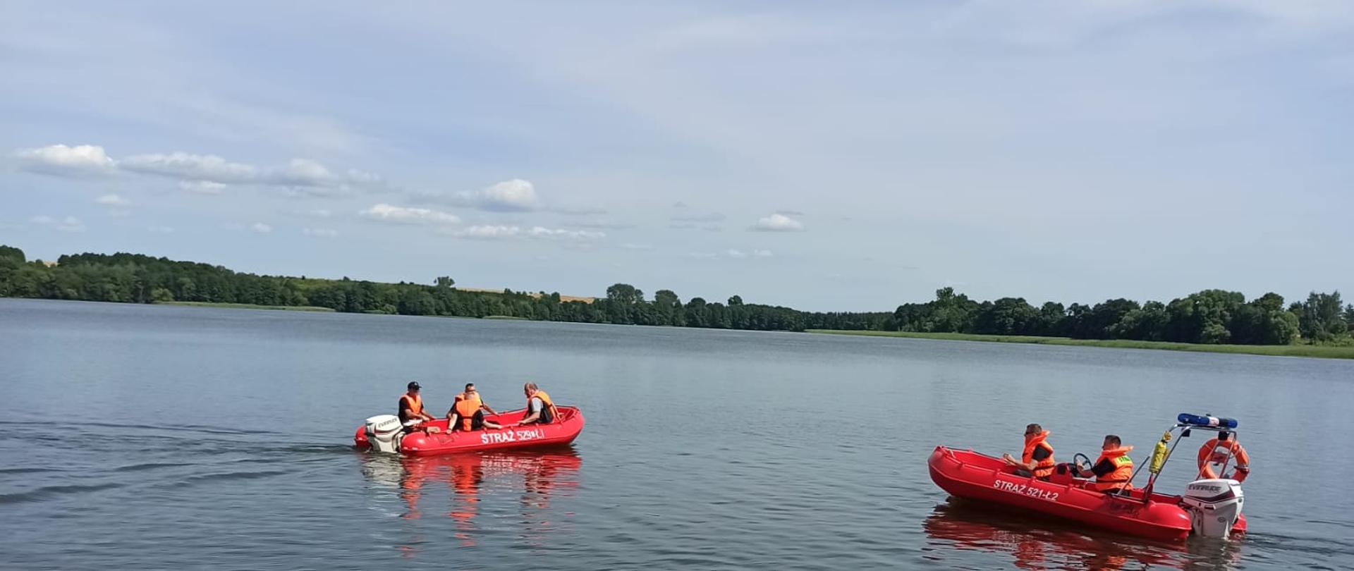 Zdjęcie wykonano w ciągu dnia, nad brzegiem zbiornika wodnego, widać na nim dwie łodzie ratownicze z załoga w kamizelkach ratowniczych.