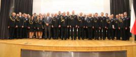 
Odznaczeni i awansowani. Strażacy w mundurach wyjściowych na scenie Auli Szkoły Aspirantów PSP w Krakowie. Zdjęcie pamiątkowe

