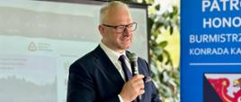Mężczyzna w garniturze, wojewoda, przemawia przez mikrofon 