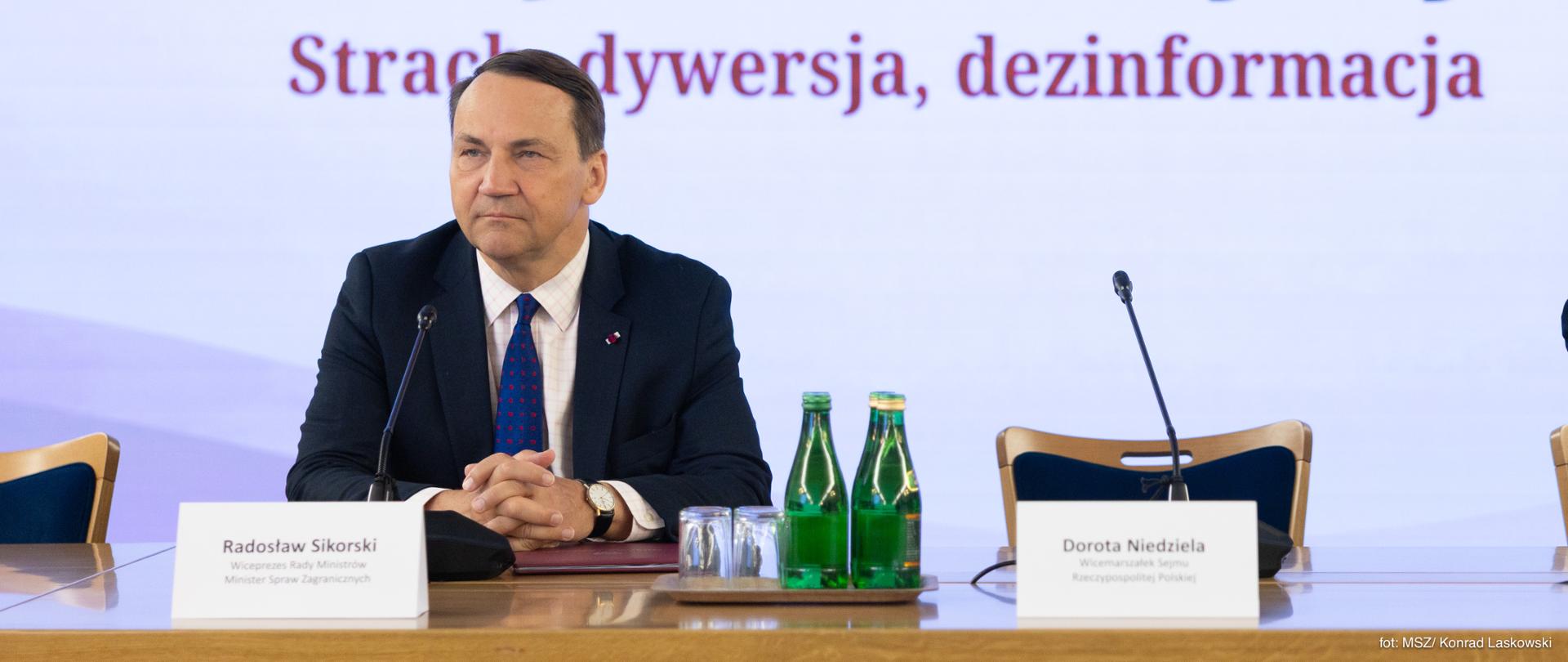 Deputy Prime Minister and Minister of Foreign Affairs Radosław Sikorski seated at the speakers’ table in front of a screen displaying the title of an event dedicated to information threats.